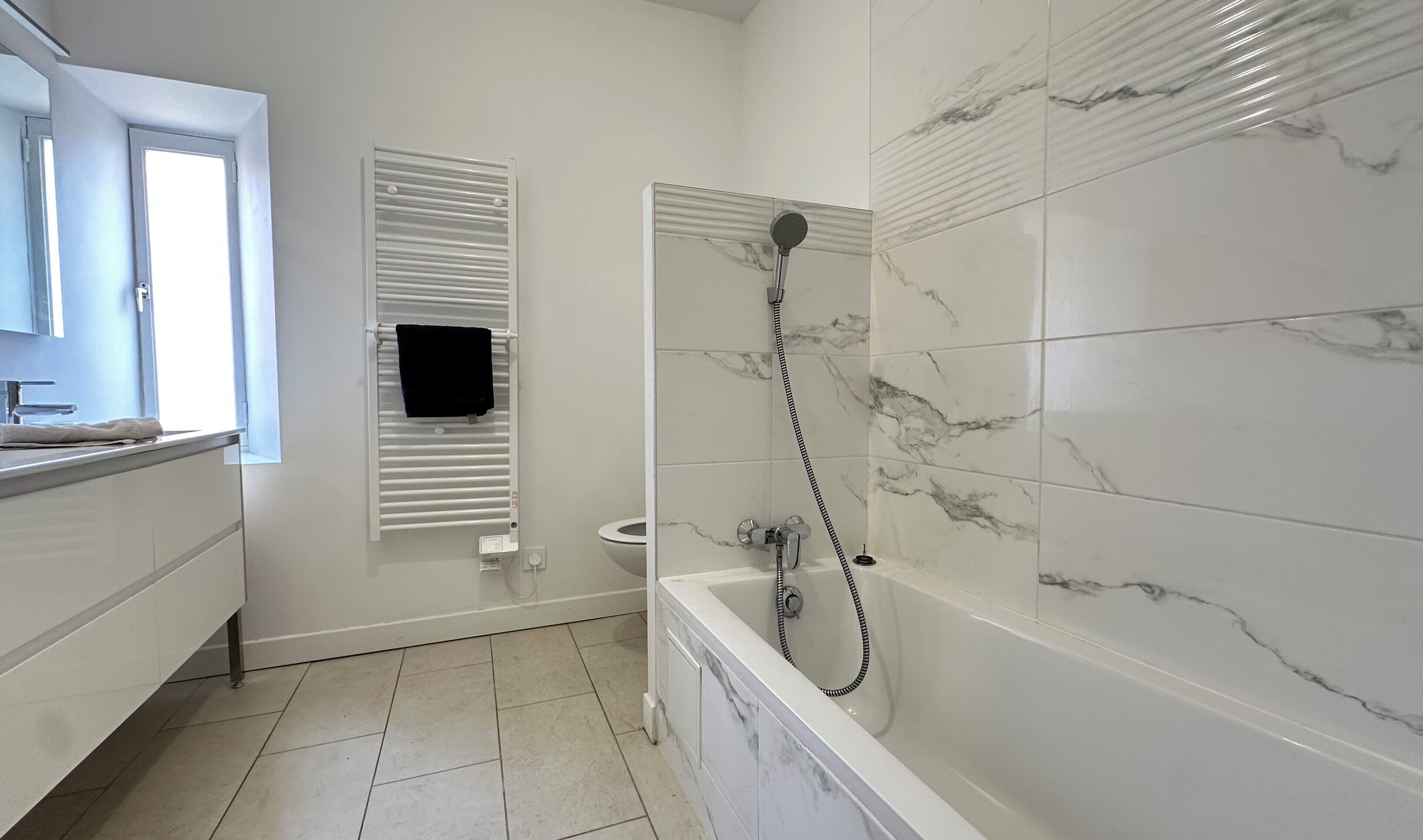 A bathroom with a bathtub, a toilet, a towel rack, and a window.