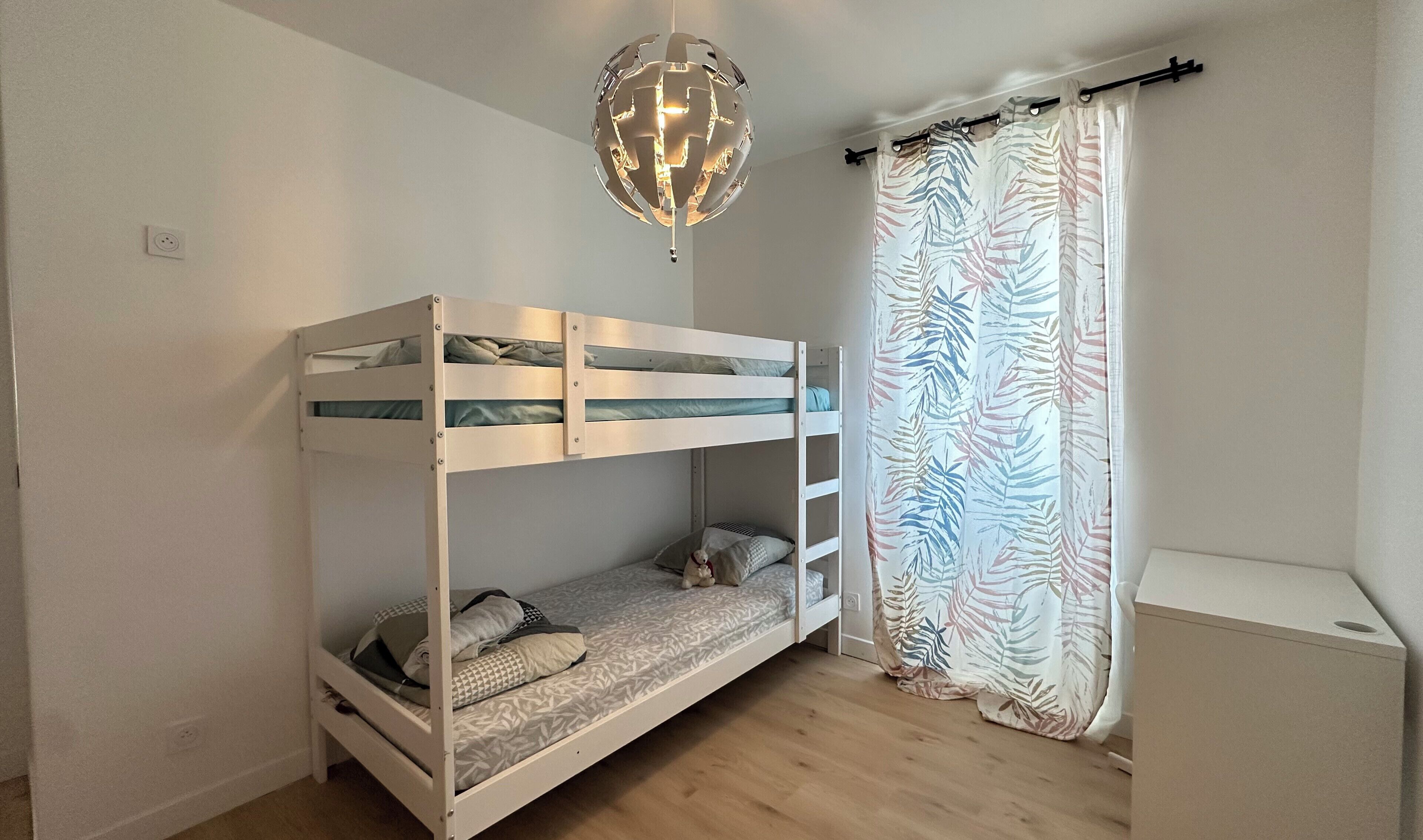 A bunk bed room with a ceiling light fixture and a patterned curtain.