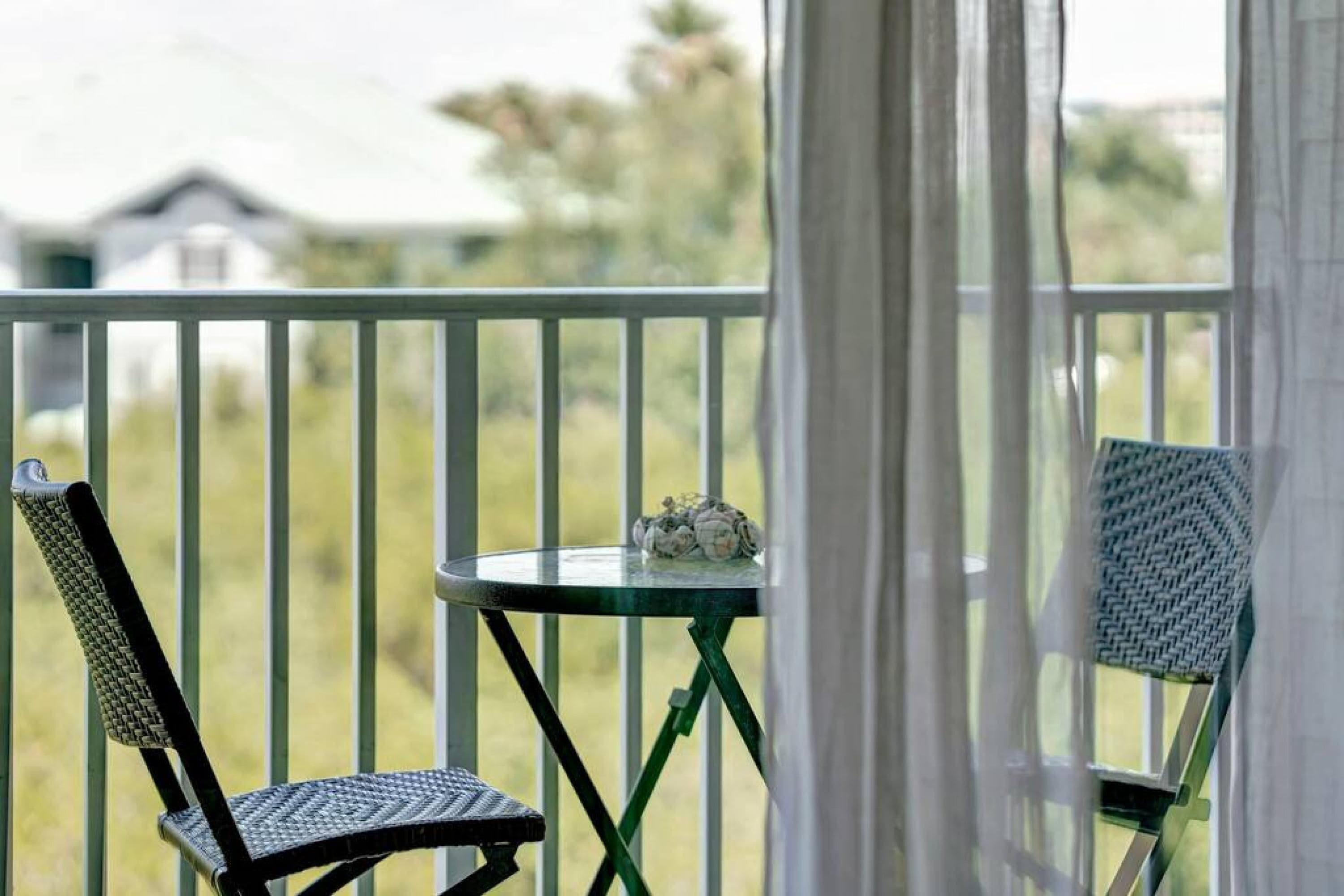 Un balcon avec deux chaises et une petite table, donnant sur un espace verdoyant avec une maison en arrière-plan.