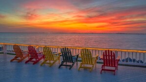 Una terraza con sillas Adirondack de colores que miran hacia una puesta de sol sobre el agua.