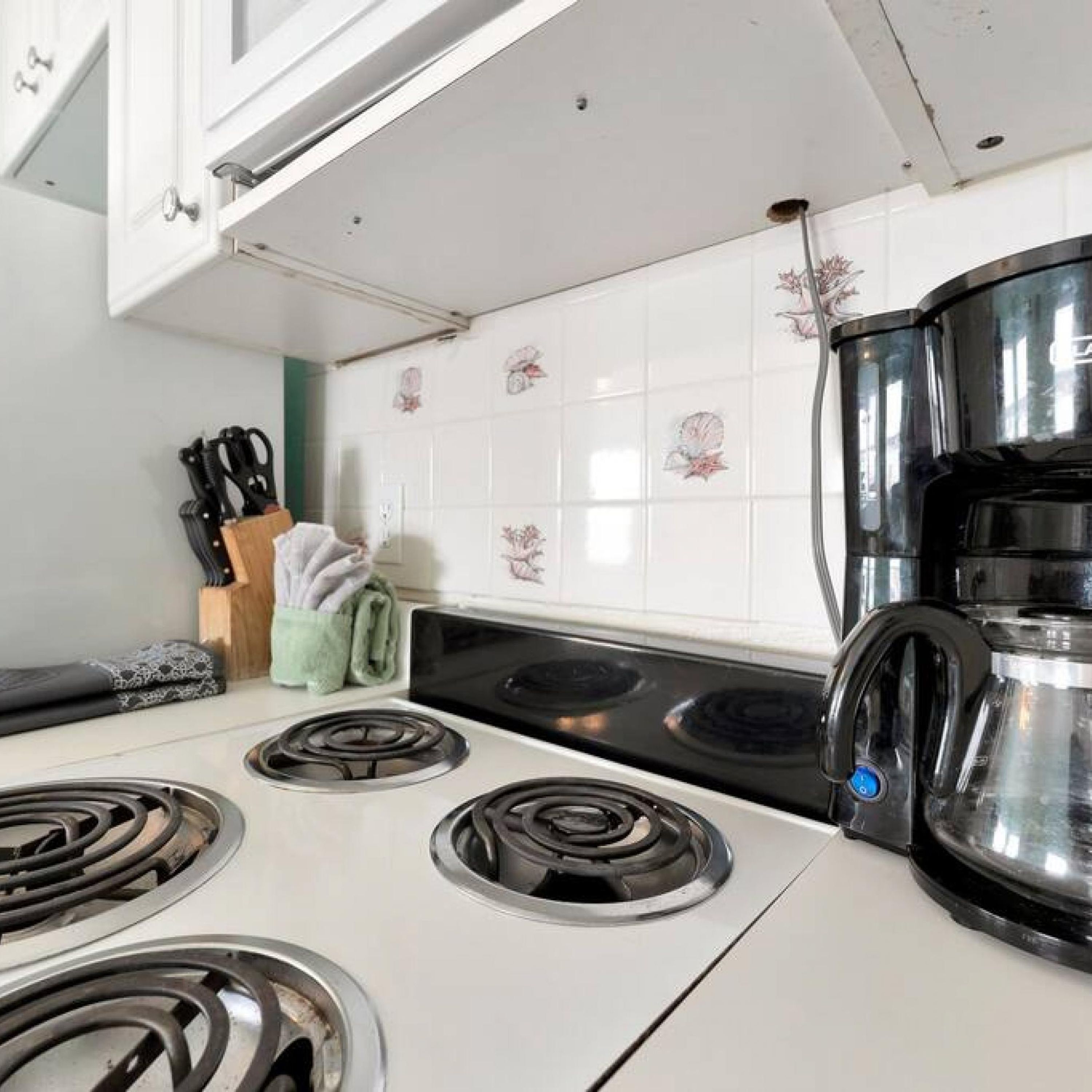 A kitchen with white cabinets, a stove, and a coffee maker.