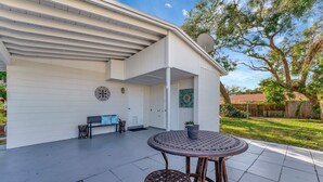 A covered patio with a round table and two stools, a bench, and a satellite dish on the roof. - The Bardmoor a Luxury Family Retreat in St Pete (Seminole)