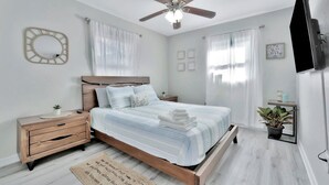 A modern bedroom with a wooden bed, a nightstand, a ceiling fan, and a TV mounted on the wall. - The Bardmoor a Luxury Family Retreat in St Pete (Seminole)