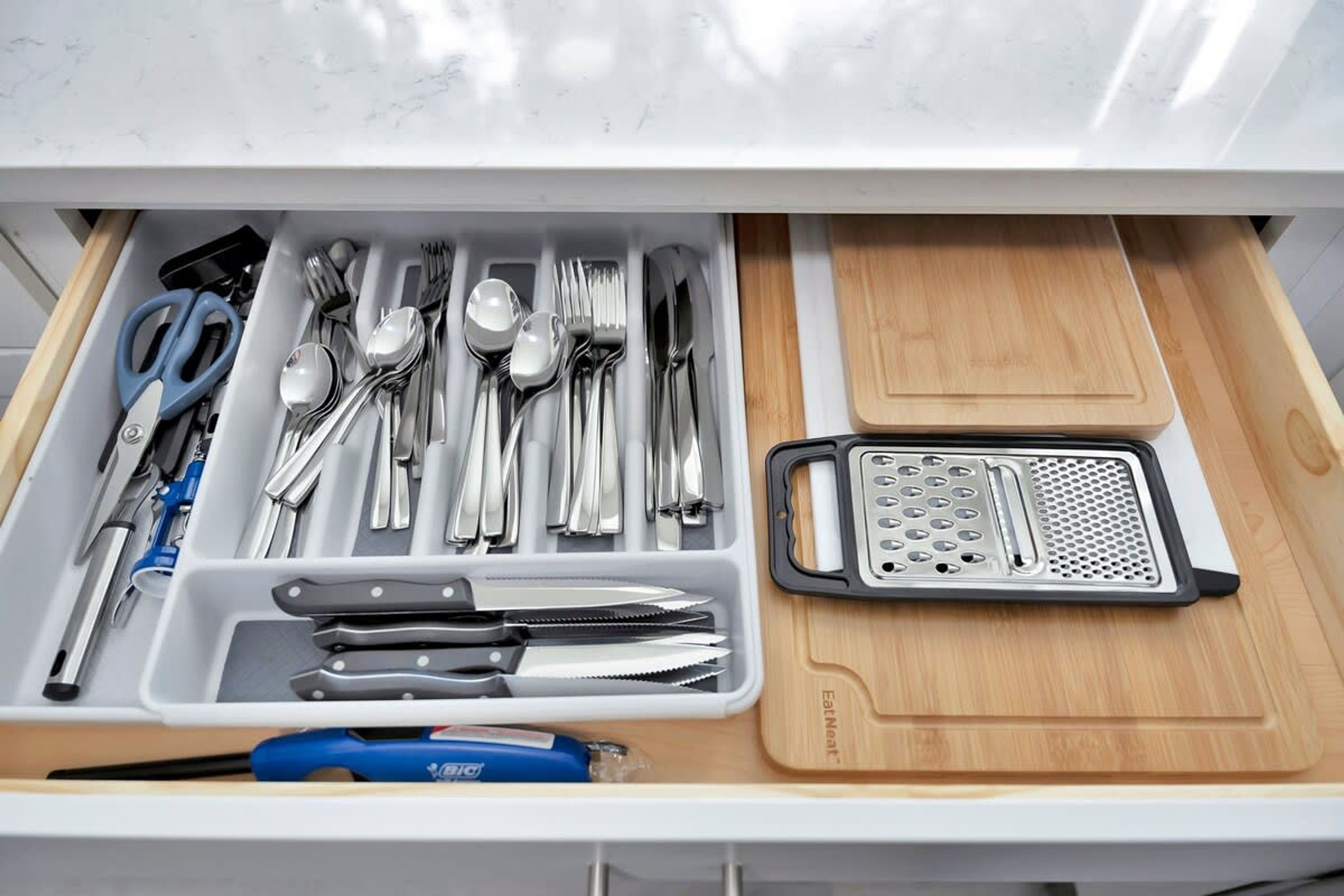 A drawer with neatly organized kitchen utensils including spoons, forks, knives, and a grater.