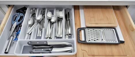 A drawer with neatly organized kitchen utensils including spoons, forks, knives, and a grater.