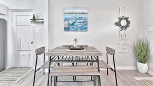 A dining area with a wooden table and chairs, a painting of boats on water, and a 'HOME' sign on the wall. - The Bardmoor a Luxury Family Retreat in St Pete (Seminole)