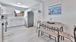 A modern kitchen with white cabinets, a grey refrigerator, and a dining area with a wooden table and bench. - The Bardmoor a Luxury Family Retreat in St Pete (Seminole)