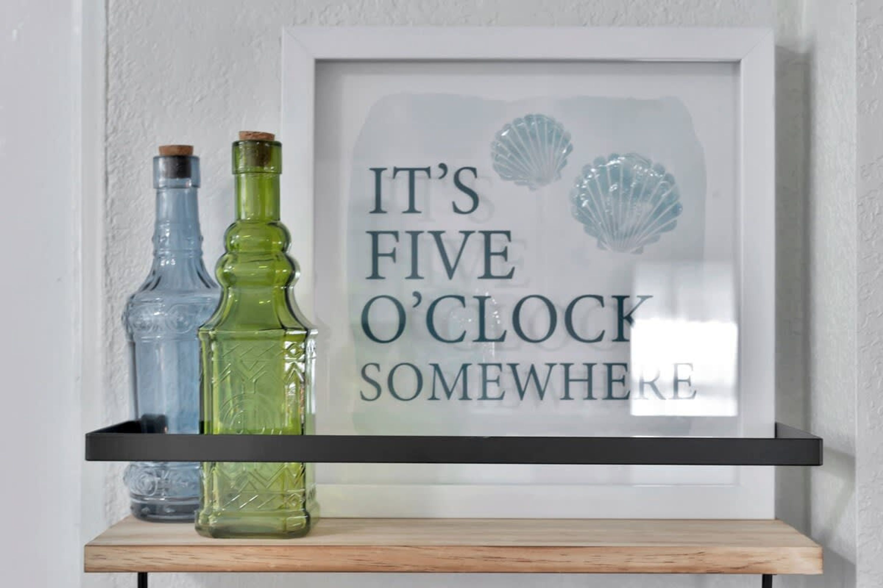 A framed quote on a wall with two bottles on a shelf below.