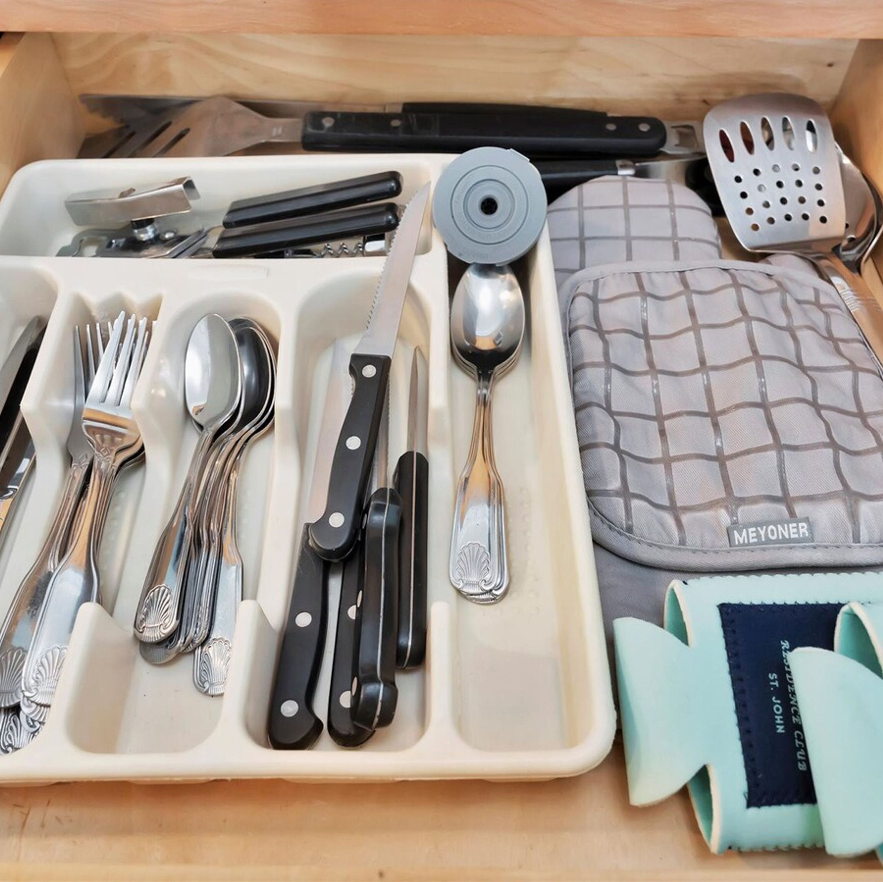 Un cajón con diferentes utensilios de cocina, como tenedores, cuchillos, cucharas y un rallador.