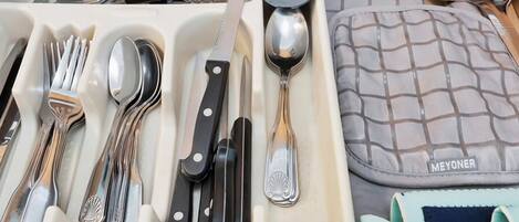 Un cajón con diferentes utensilios de cocina, como tenedores, cuchillos, cucharas y un rallador.