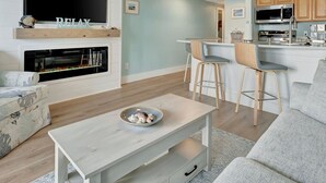 A modern living room with a fireplace, a dining area with bar stools, and a kitchen with wooden cabinets and a microwave. - Oceans Pointe Nantucket Inspired Condo on the bay (Tampa)
