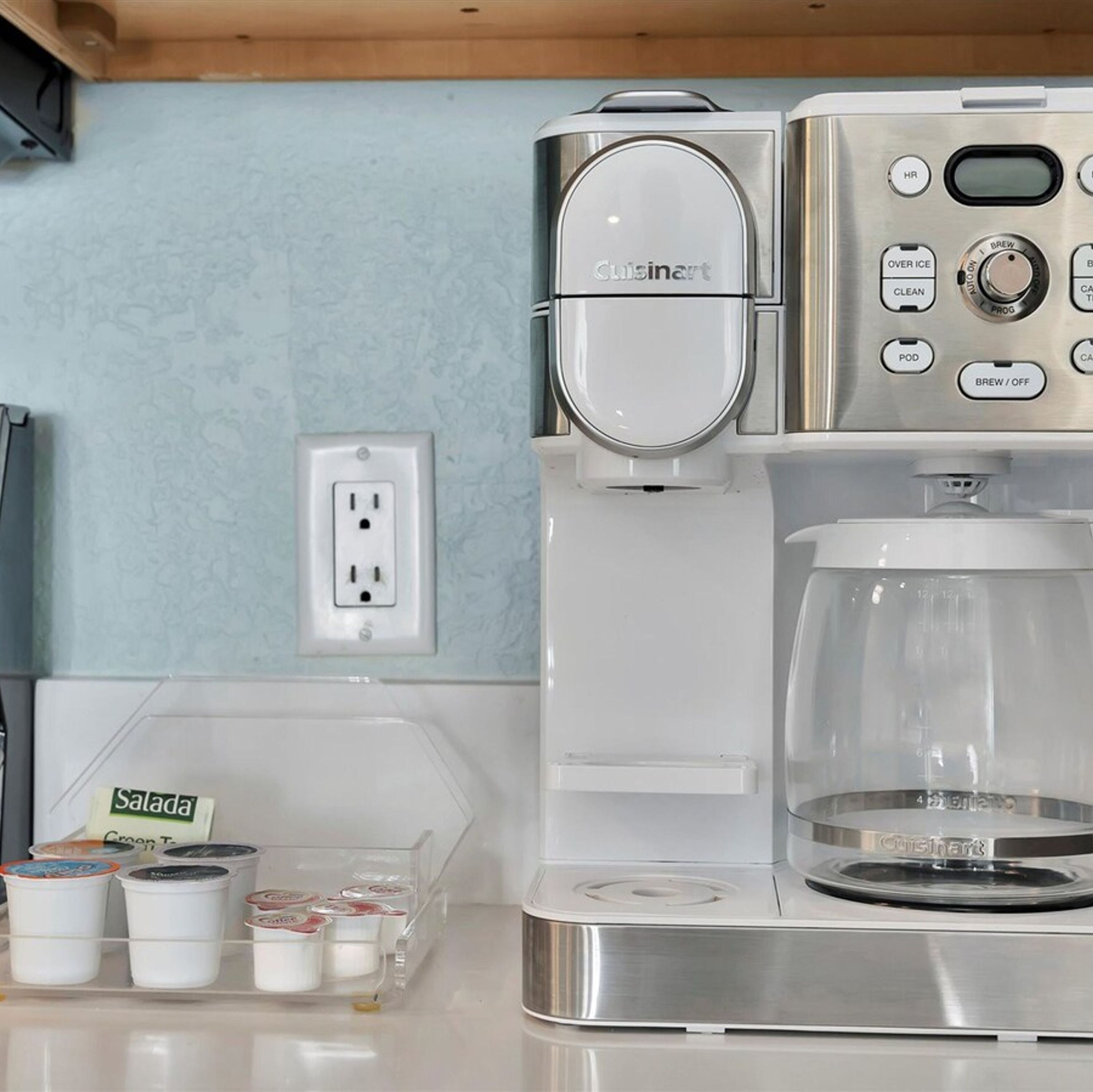 Une cuisine équipée d’une machine à café, d’une cafetière et d’un récipient contenant des dosettes de café.