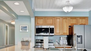 A modern kitchen with wooden cabinets, stainless steel appliances, a central island with bar stools, and a chandelier. - Oceans Pointe Nantucket Inspired Condo on the bay (Tampa)
