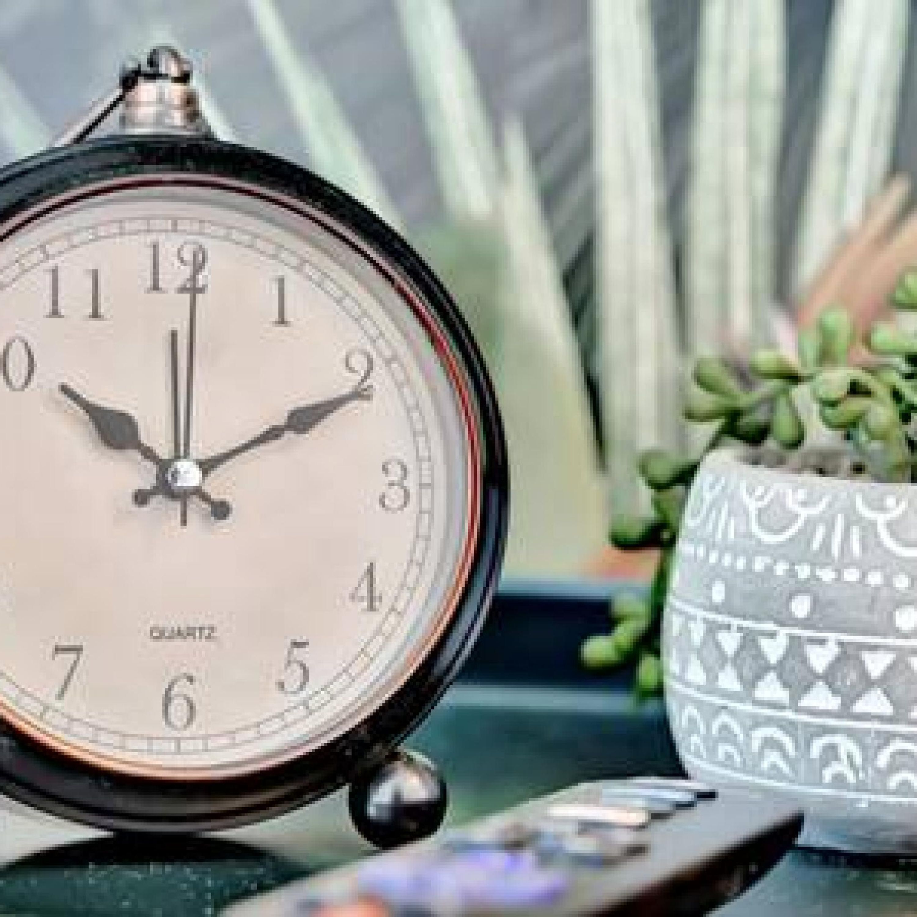 Un réveil à quartz avec un boîtier noir et un cadran blanc, posé sur une table avec un bol décoratif et une télécommande.