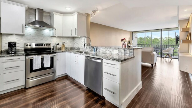A modern kitchen with stainless steel appliances, white cabinetry, and a marble countertop.