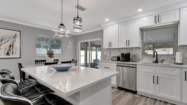 A modern kitchen with white cabinets, a central island, black bar stools, pendant lighting, and a view to the outside.