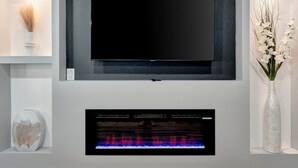 A modern living room with a flat-screen TV mounted on a grey wall, a built-in fireplace below, and decorative items on shelves.