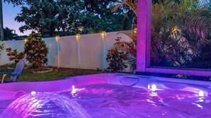 A hot tub with purple lighting, surrounded by a white fence and various plants.