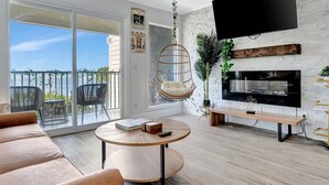 Un salon moderne doté d’un grand téléviseur, d’une cheminée et d’un balcon aménagé avec du mobilier d’extérieur.