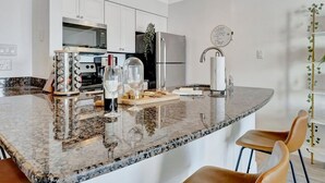 Une cuisine moderne avec des armoires blanches, des appareils en acier inoxydable, un comptoir en granit et un coin salon avec deux fauteuils en cuir.
