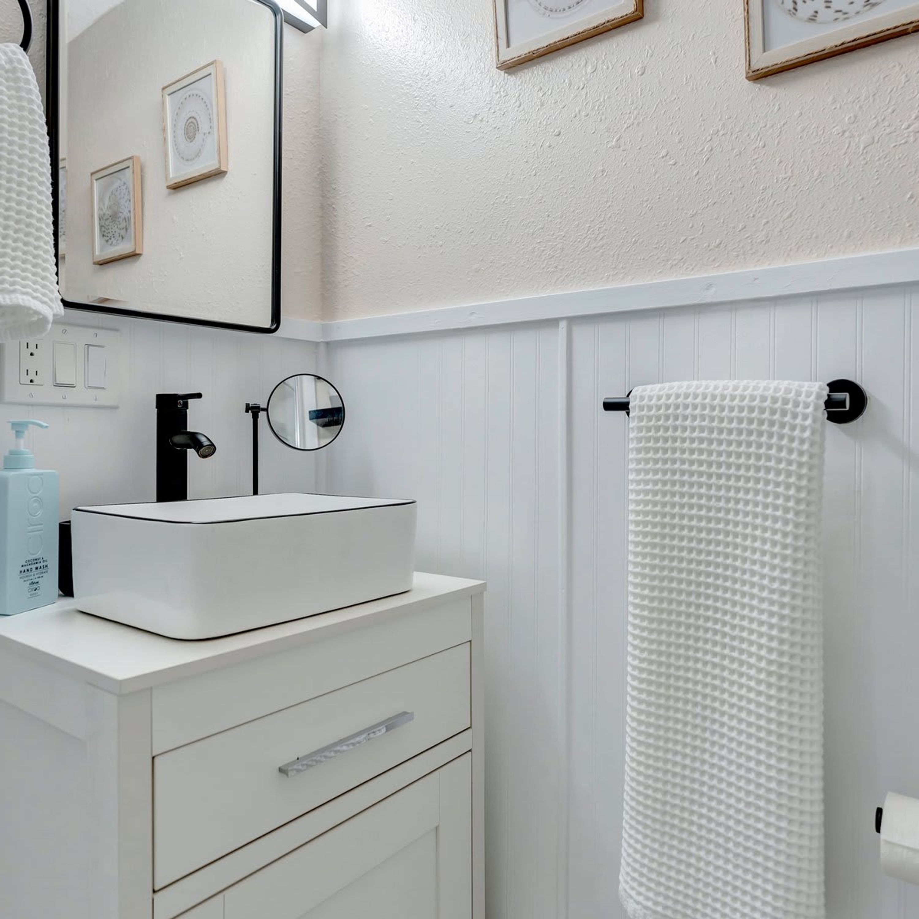 A bathroom with a white sink, a mirror, a towel rack, and framed pictures on the wall.