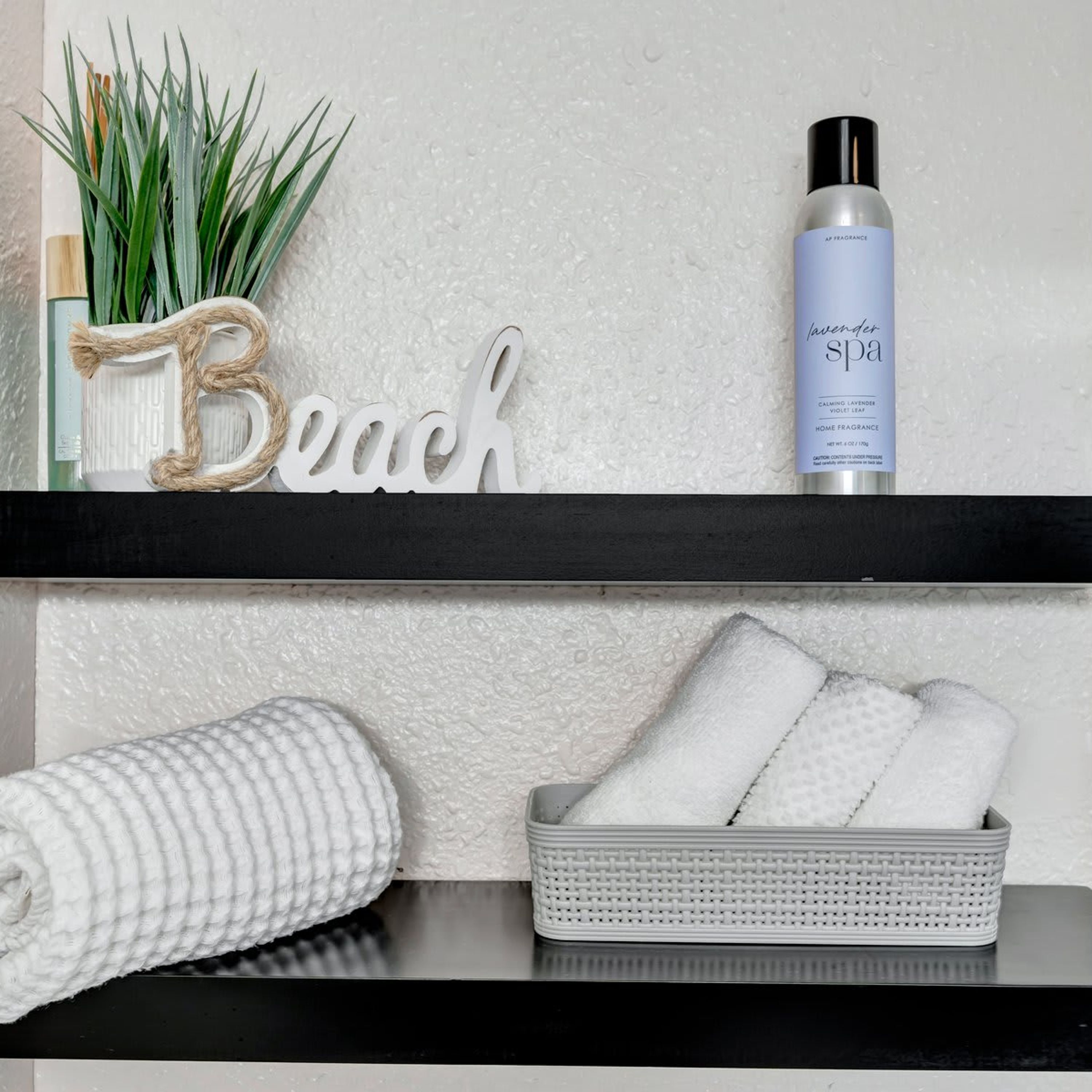 Een plank met een plant, een fles lavendel badproduct en het woord 'Beach' in sierletters.