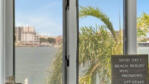 Ein Fenster mit Blick auf ein Gewässer, Palmen und einem Schild mit Text.