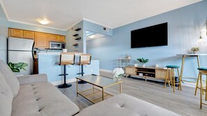 A modern living room with a sofa, coffee table, and a kitchen area with a refrigerator, microwave, and bar stools. - Serenity on the Sea Luxury Condo w Prvt Balcony (Tampa)
