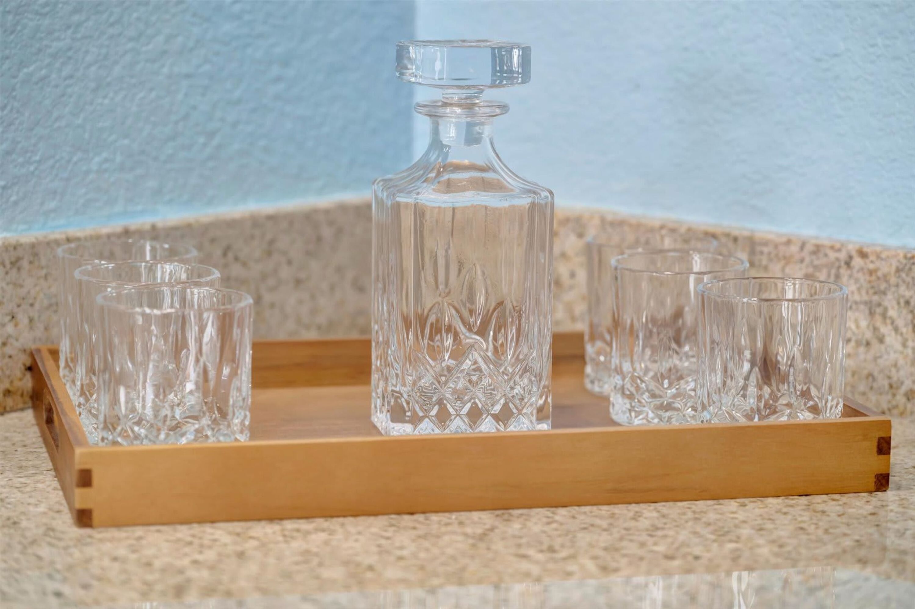 Ein Holztablett mit einer Glaskaraffe und vier Gläsern auf einer strukturierten Oberfläche.