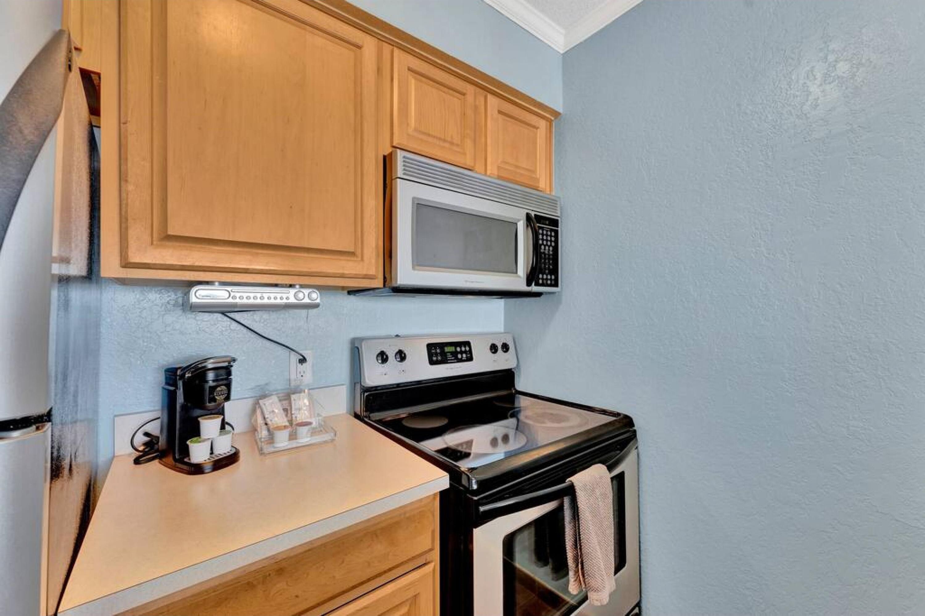 A compact kitchen with wooden cabinets, a microwave, a stove, and a coffee maker.