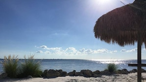 A beach with a thatched umbrella, clear blue sky, and calm sea. - Serenity on the Sea Luxury Condo w Prvt Balcony (Tampa)