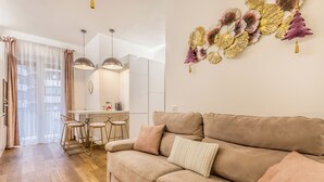 Una sala moderna con un sofá color beige, una zona de comedor con una mesa y sillas blancas, y un adorno en la pared.
