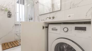Un bagno moderno con una lavatrice Bosch, pareti in marmo e box doccia in vetro.