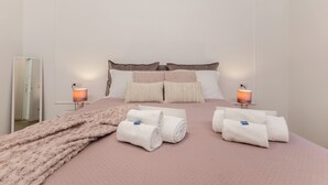 Una cama bien hecha con una colcha rosa, dos lámparas de noche y toallas enrolladas sobre la cama.