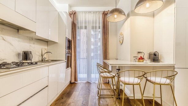Una cocina moderna con armarios blancos, encimera de madera y una zona de comedor con dos taburetes tipo bar.
