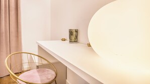 Una habitación con un escritorio blanco, un espejo grande, una silla dorada y un pequeño jarrón decorativo.