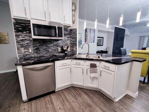 A modern kitchen with white cabinets, a black countertop, a built-in microwave, and a dishwasher. - Entire Luxury 3 Bedroom Residential House (McKinney)