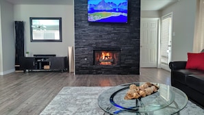 Een moderne woonkamer met een stenen open haard, een flatscreen televisie erboven en een glazen salontafel met decoratieve objecten.