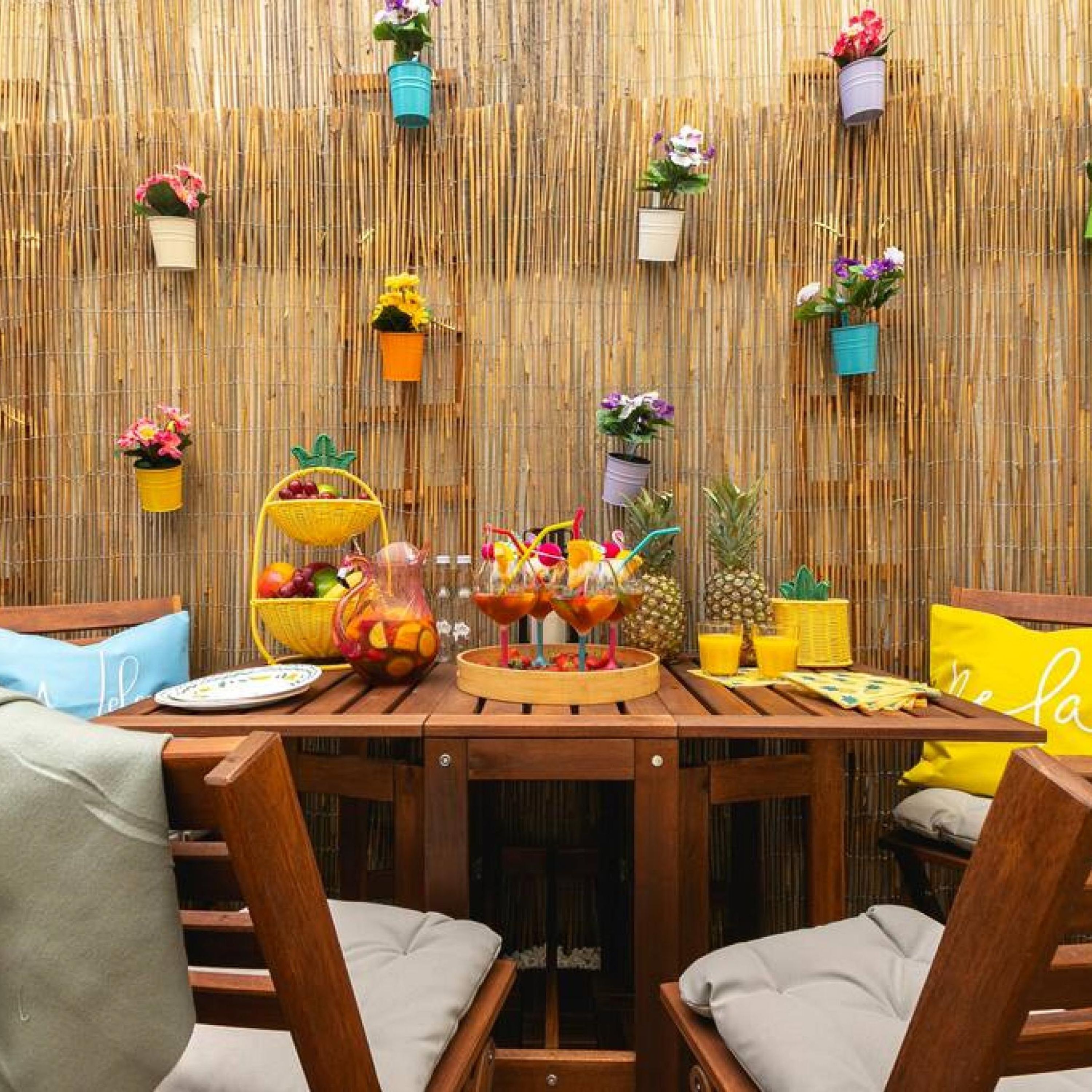 A wooden dining table with chairs, a bamboo wall, and various potted plants and fruit baskets.
