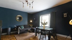 A modern living room with a dark blue wall, a round mirror, a chandelier, a dining table with chairs, and a sofa. - Designer Retreat 5 Location Balcony Parking (Hove)