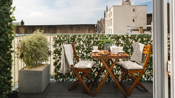 A wooden deck with a table and two chairs, surrounded by greenery and a white fence. - Designer Retreat 5 Location Balcony Parking (Hove)