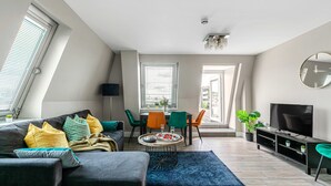 A modern living room with a sofa, dining table, chairs, a TV, and a potted plant. - The Lanes Gem Penthouse Rooftop Terrace Sea View (Brighton)
