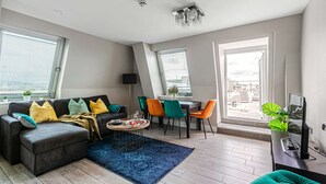 A modern living room with a grey sofa, colorful chairs, a dining table, and large windows. - The Lanes Gem Penthouse Rooftop Terrace Sea View (Brighton)