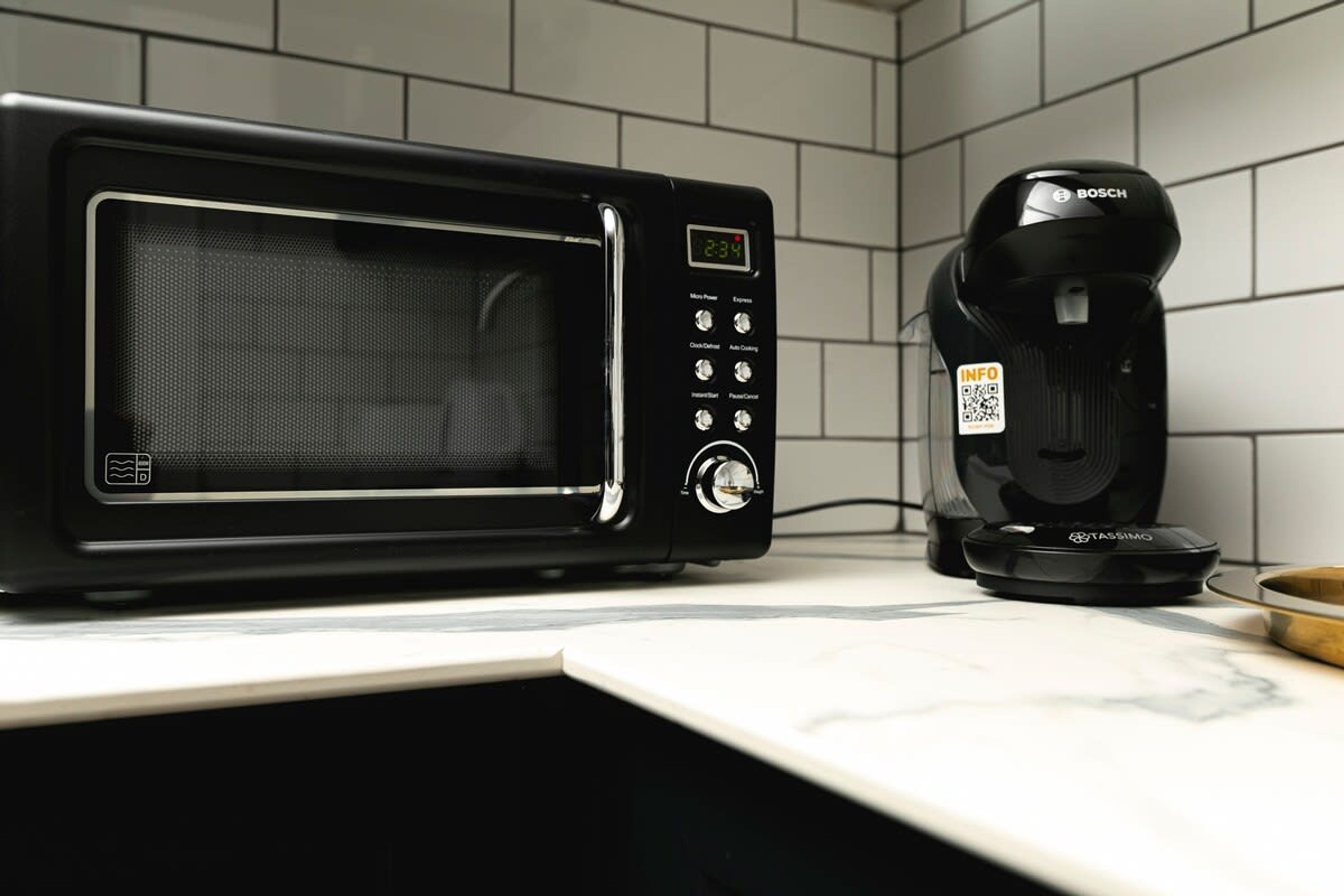 Une cuisine avec un micro-ondes noir et une machine à café posés sur le plan de travail.