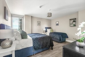 A bedroom with two beds, a nightstand, a lamp, a decorative vase, and framed pictures on the wall.