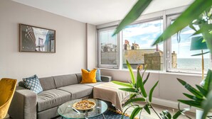 A modern living room with a sofa, a glass coffee table, and a view of the cityscape through large windows. - Brighton Lanes Sea View 2BR AP (Brighton)