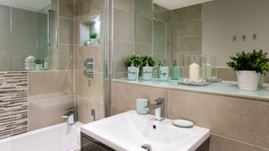 A modern bathroom with a large mirror, a bathtub, and a sink. There are toiletries on the countertop and a potted plant on the wall. - Brighton Lanes Sea View 2BR AP (Brighton)