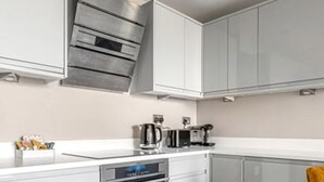 A modern kitchen with white cabinetry, a built-in oven, and a stainless steel range hood. - Brighton Lanes Sea View 2BR AP (Brighton)