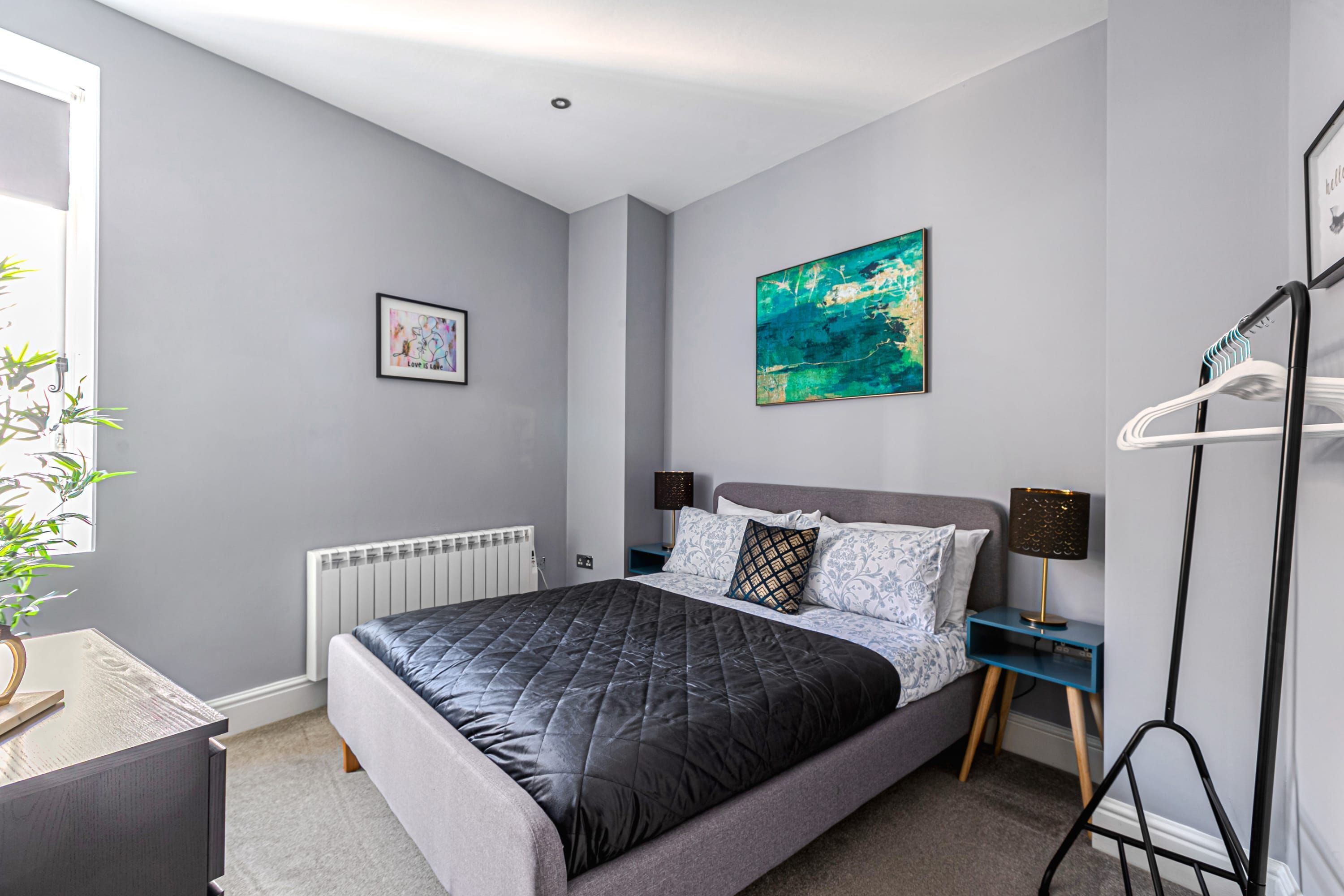 Ein modernes Schlafzimmer mit einem großen Bett, einem Nachttisch, einem Heizkörper und einem an der Wand befestigten Regal.