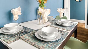 A dining area with a long table set for four, a wall clock, and a vase with flowers. - The Lanes Getaway Moments Away From Pier Beach (Brighton)